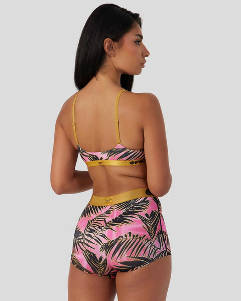 Woman wearing pink and black palm leaf print bikini set with yellow trim, shown from back.