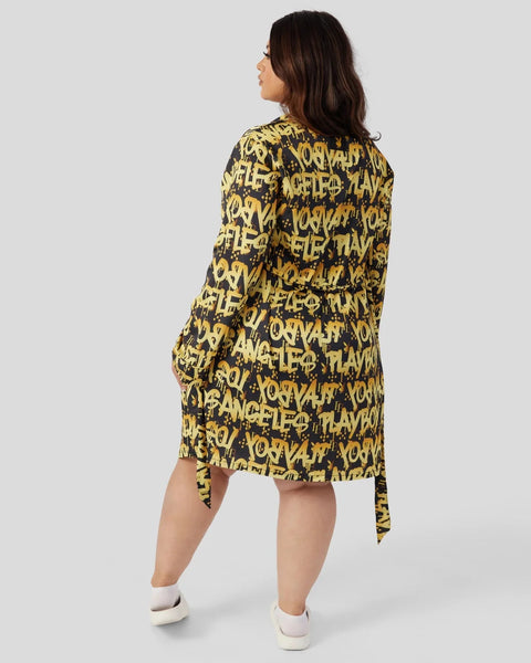 Woman wearing black and gold graffiti-print shirt dress with long sleeves and asymmetrical hem, shown from back.