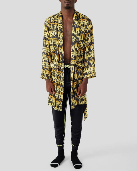 Man wearing yellow and black graffiti-patterned robe with black joggers and socks.