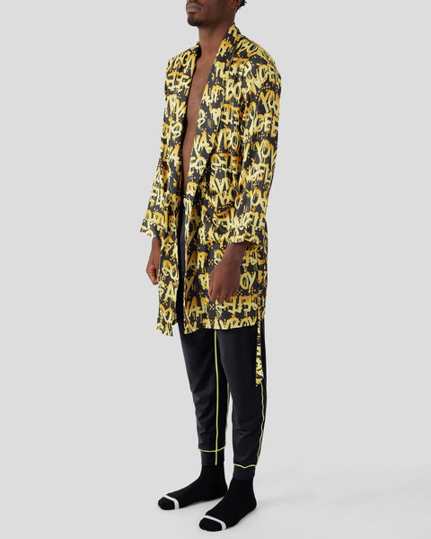 Man wearing yellow and black graffiti-print open robe over black pants with yellow stripe detail and black socks.