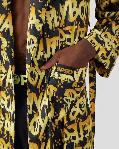 Black and gold graffiti-patterned garment with PSD branding on waistband, shown on model with hand in pocket.