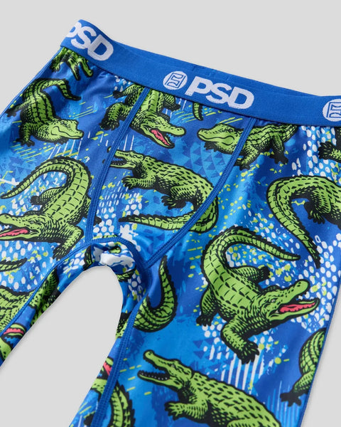 Blue briefs with lime green alligator print, PSD waistband, and abstract geometric pattern background.