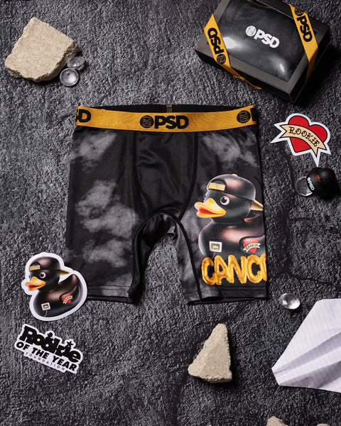Black PSD boxer briefs with yellow waistband and duck graphic print, displayed flat with matching packaging and accessories.