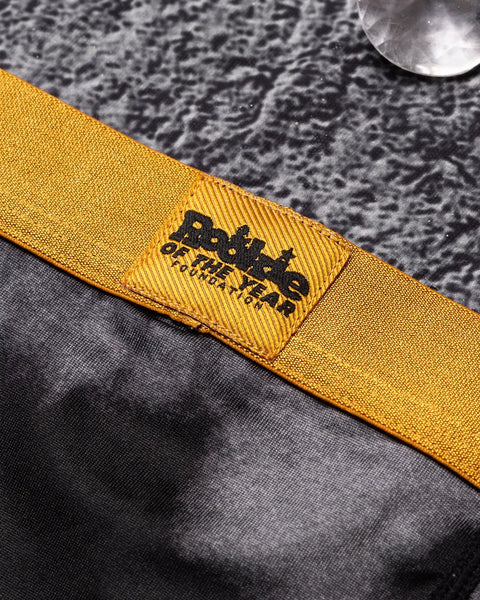Yellow fabric strap with black woven label featuring text, laid on gray textured material.