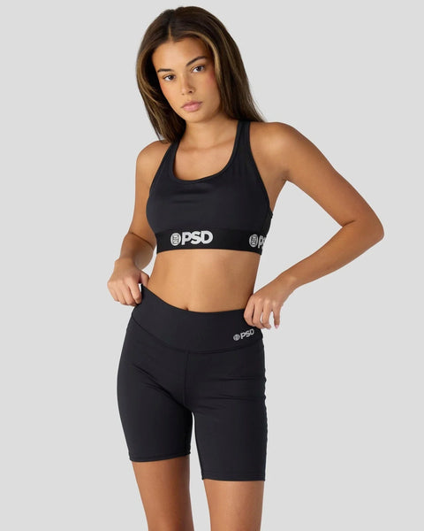 Woman wearing black sports bra and bike shorts with PSD branding on elastic waistbands.