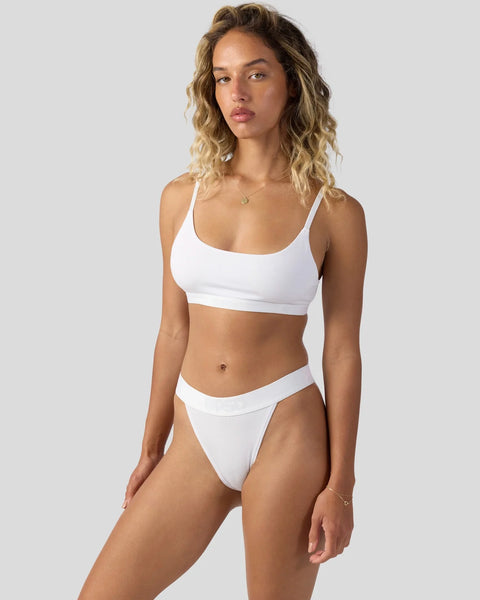 Woman wearing white modal sports bra and matching bikini briefs with thin straps against neutral background.