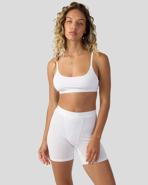 Woman wearing white modal sports bra with scoop neckline and matching white modal shorts.
