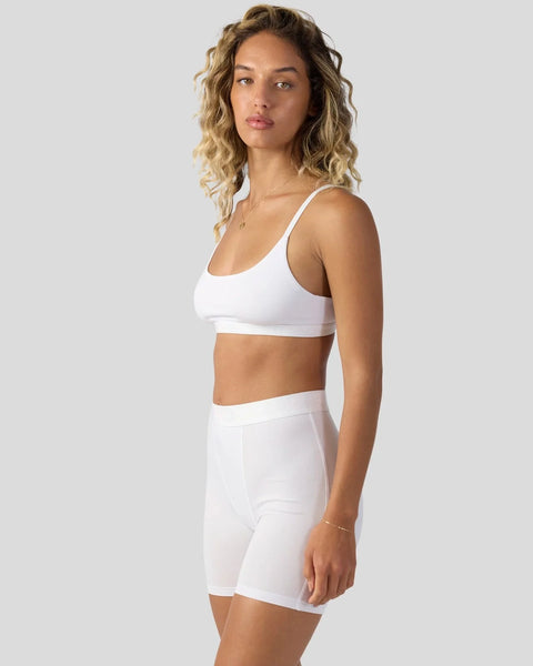 Woman wearing white sports bra and matching high-waist shorts against neutral background.