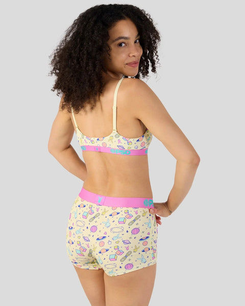 Woman wearing yellow modal bra and shorts set with colorful space-themed icons and pink trim.