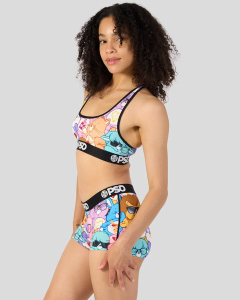 Woman wearing Care Bears sports bra and shorts set with colorful character print and black branded waistband.