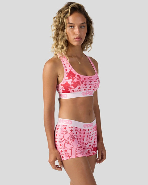 Woman wearing pink Looney Tunes print sports bra and matching shorts with character graphics and geometric patterns.
