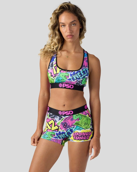 Woman wearing colorful Looney Tunes-patterned sports bra and shorts set with black PSD waistbands.