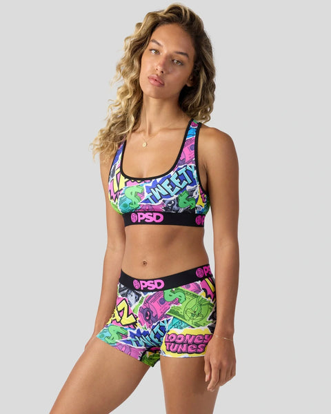 Woman wearing colorful Looney Tunes-printed sports bra and shorts set with neon graphics and PSD waistband.