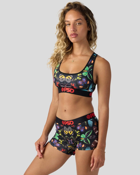 Woman wearing black sports bra and matching shorts with colorful butterfly and insect print design.