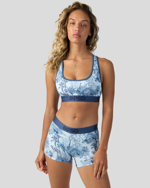 Woman wearing blue and white toile-print sports bra and matching shorts with navy waistbands.