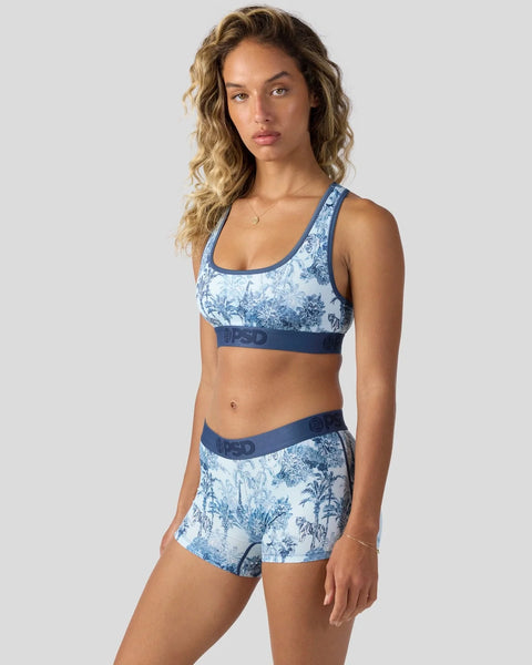 Woman wearing blue and white toile-printed sports bra and matching shorts with navy elastic bands.