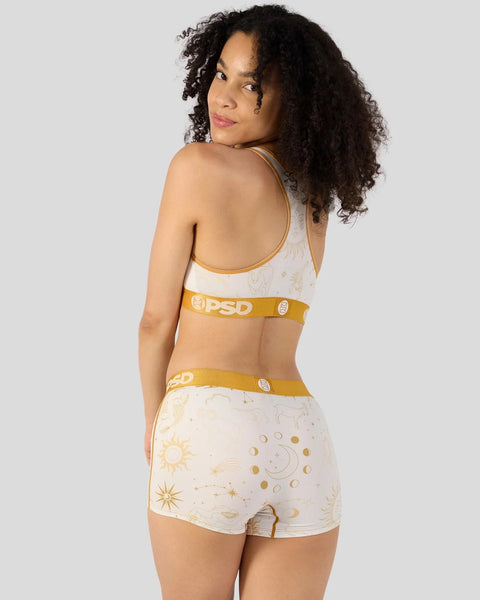 Woman wearing white and gold astrology-patterned sports bra and shorts with gold waistbands.