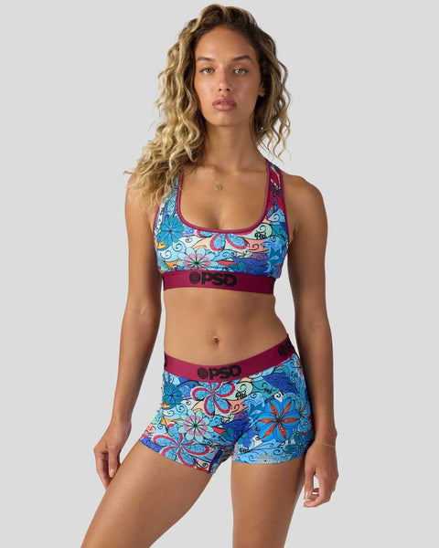 Woman wearing colorful floral print sports bra and shorts set with burgundy trim and branding.