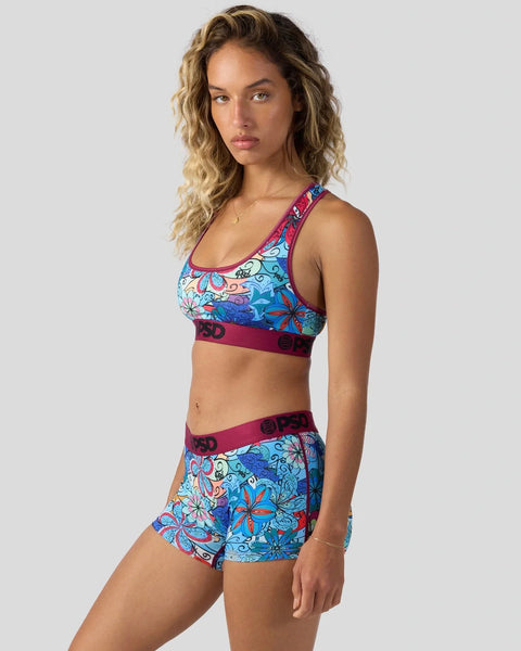 Woman wearing colorful psychedelic floral print sports bra and matching shorts with burgundy bands.
