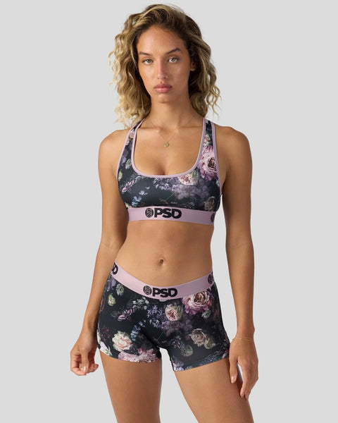 Woman wearing dark floral sports bra and shorts set with pink waistband and PSD branding.