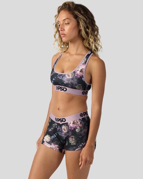 Woman wearing dark floral sports bra and shorts set with pink and purple rose print and PSD branding.