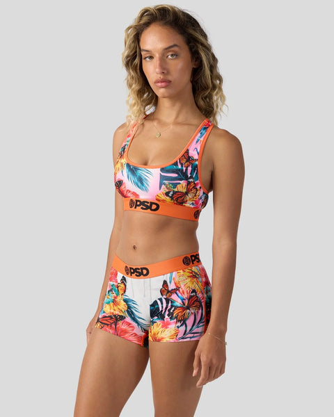 Woman wearing tropical floral sports bra and shorts set with orange waistband details.