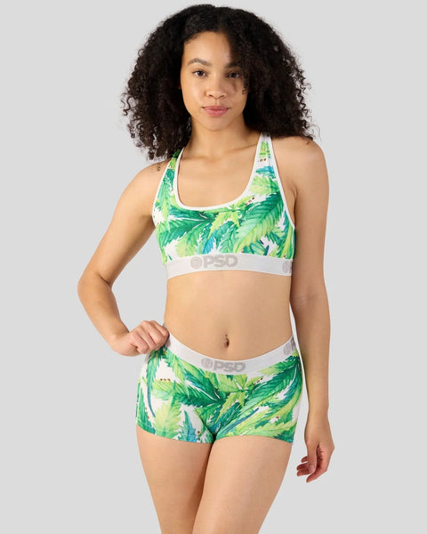 Woman wearing green and white leaf-print sports bra and matching shorts set with white waistband.