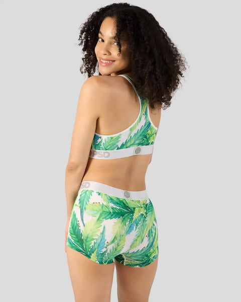 Woman wearing green leaf-patterned sports bra and matching boy shorts with white waistbands, shown from behind.