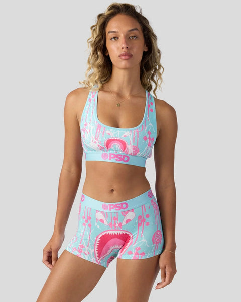 Woman wearing turquoise and pink patterned sports bra and shorts set with matching waistband design.