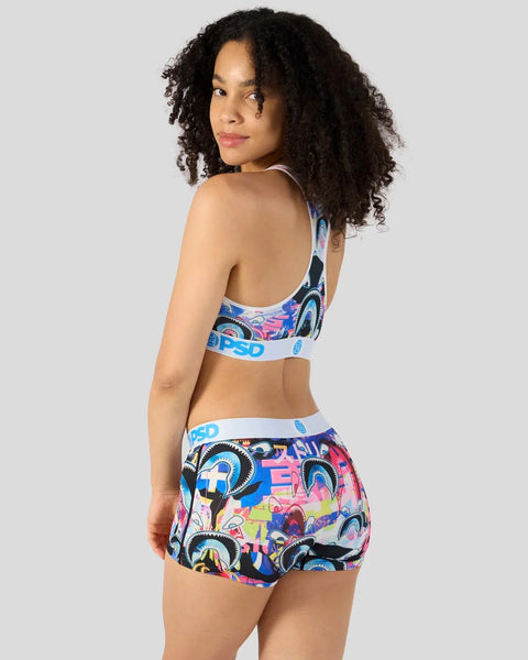 Woman wearing colorful shark-print sports bra and matching shorts with blue waistband trim.