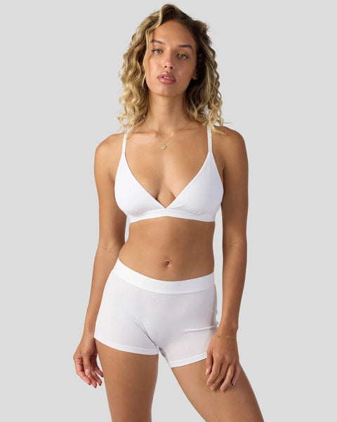 Woman wearing white modal sports bra with matching white shorts against neutral background.