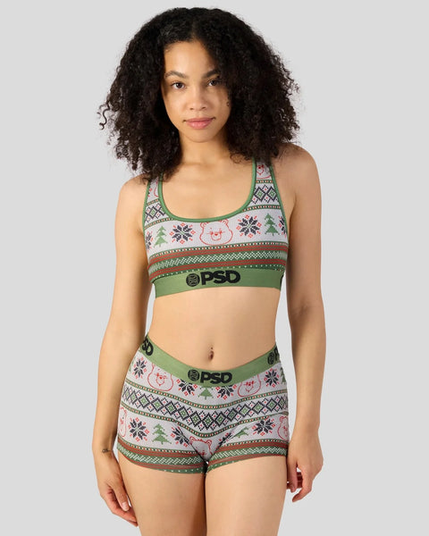 Woman wearing green and cream ugly sweater-patterned sports bra and matching shorts with Care Bears and holiday motifs.