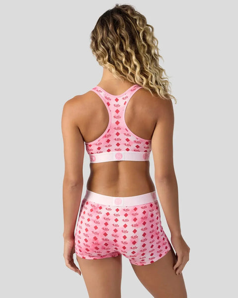 Woman wearing pink sports bra and shorts with red repeating diamond and text pattern, back view.