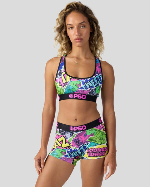 Woman wearing colorful Looney Tunes-printed sports bra and shorts set with neon graphic patterns and black PSD waistbands.