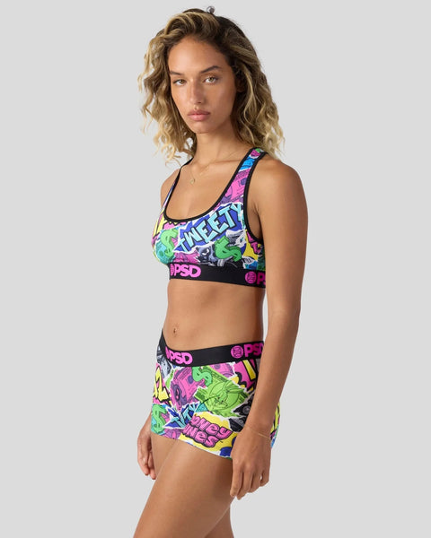 Woman wearing colorful neon Looney Tunes sports bra and shorts set with graphic print and black waistband.