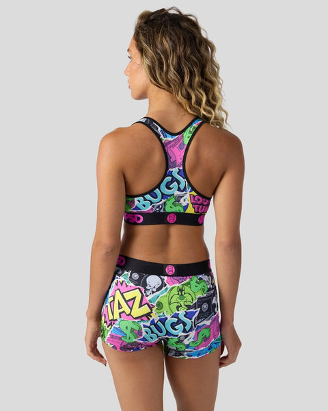 Woman wearing colorful Looney Tunes-themed sports bra and shorts with neon graphic print and text design.