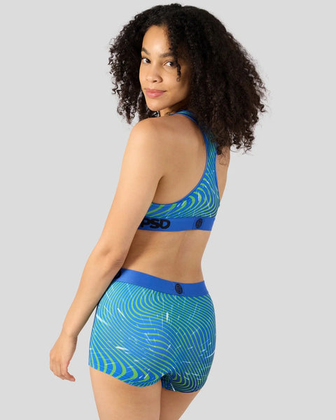 Woman wearing blue sports bra and shorts with lime green swirl pattern and blue waistband.