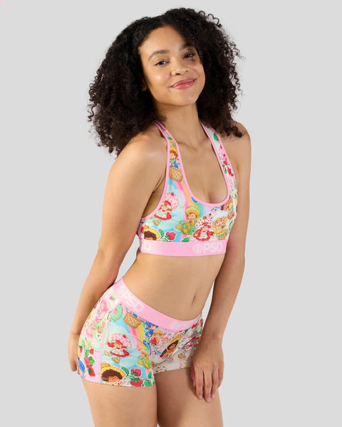 Woman wearing pastel pink and multicolor fruit-patterned halter bikini top and matching shorts.