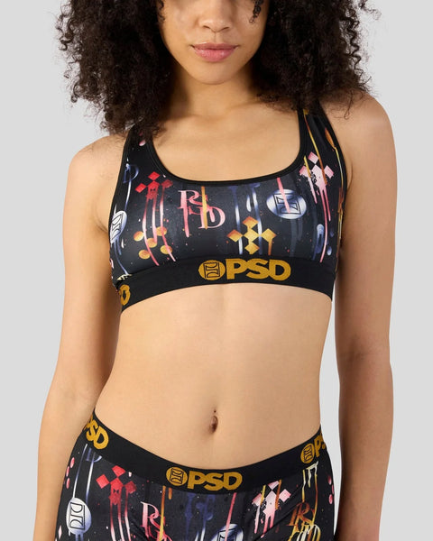 Black sports bra with colorful geometric and abstract print, gold PSD branding, and thin shoulder straps.