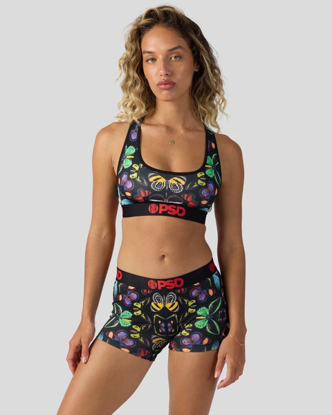 Woman wearing black sports bra and shorts with colorful floral and butterfly print and red PSD branding.