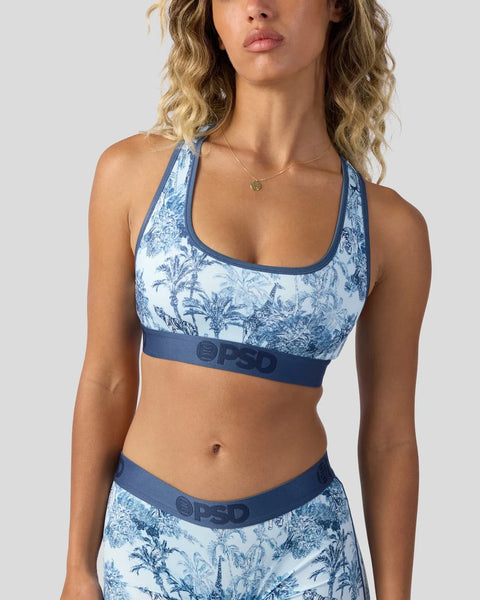 Woman wearing blue and white botanical print sports bra with matching waistband and pendant necklace.