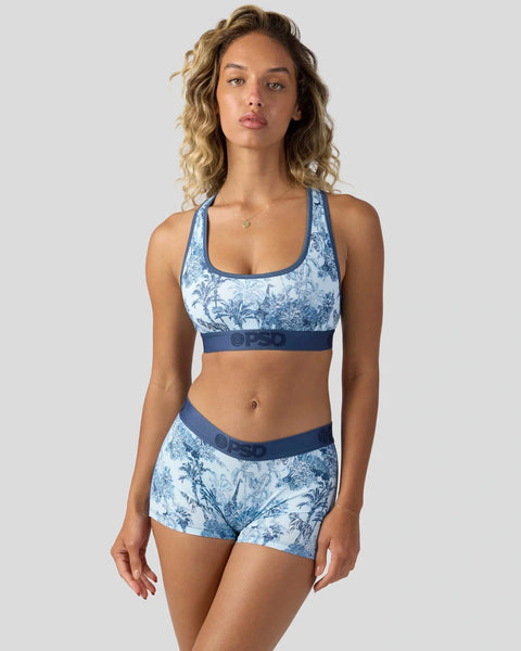 Woman wearing blue and white floral sports bra and matching shorts set with navy trim.