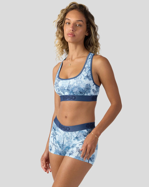 Woman wearing blue and white floral print sports bra and matching shorts set with navy trim.