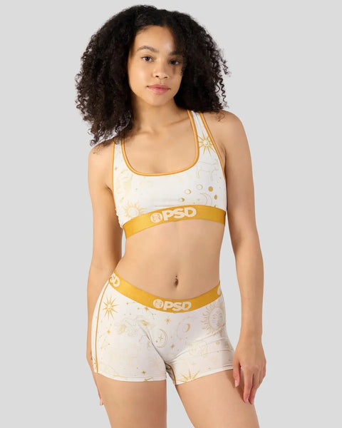 Woman wearing cream and gold astrology-themed sports bra and shorts set with sun and moon print.