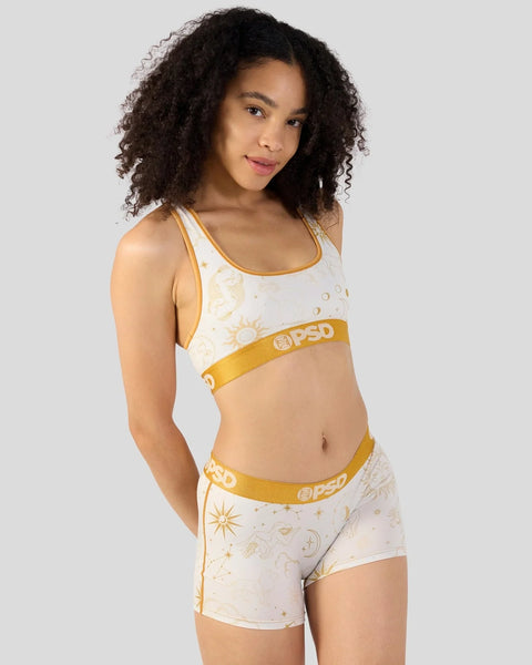 Woman wearing white and gold celestial-print sports bra and matching shorts with gold elastic waistband.