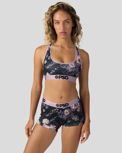 Woman wearing dark floral sports bra and matching shorts with pink trim and PSD branding.