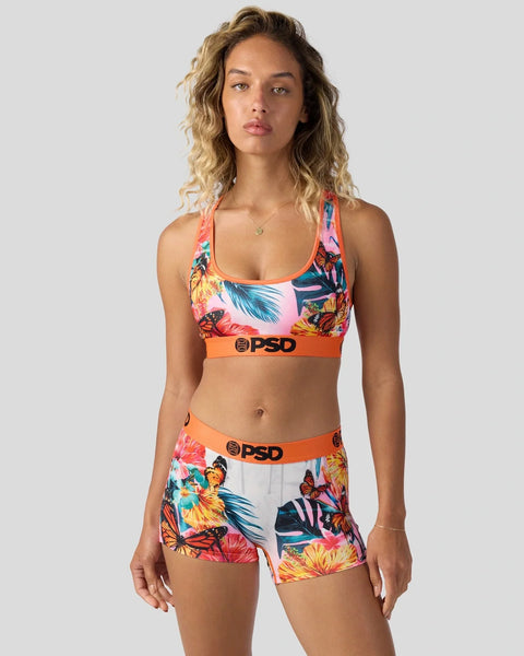 Woman wearing multicolored tropical print sports bra and matching shorts with orange trim and PSD branding.