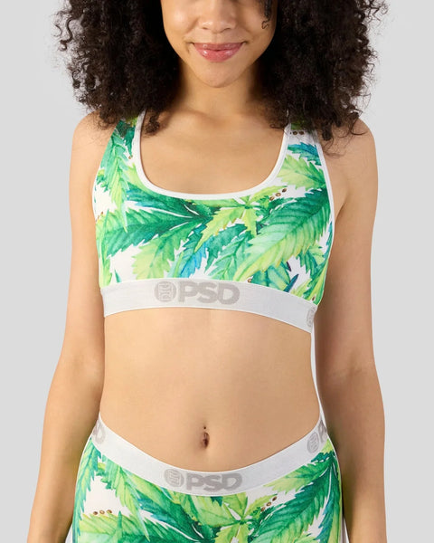 Woman wearing white sports bra and matching waistband with green and yellow leaf print pattern.