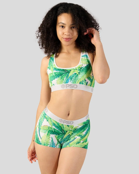Woman wearing green and white leaf-print sports bra and matching shorts with white waistband.