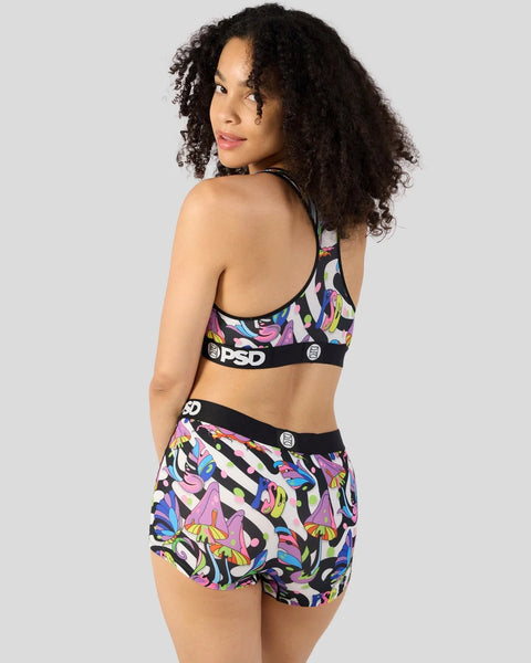 Woman wearing PSD sports bra and shorts with colorful mushroom print on black background.